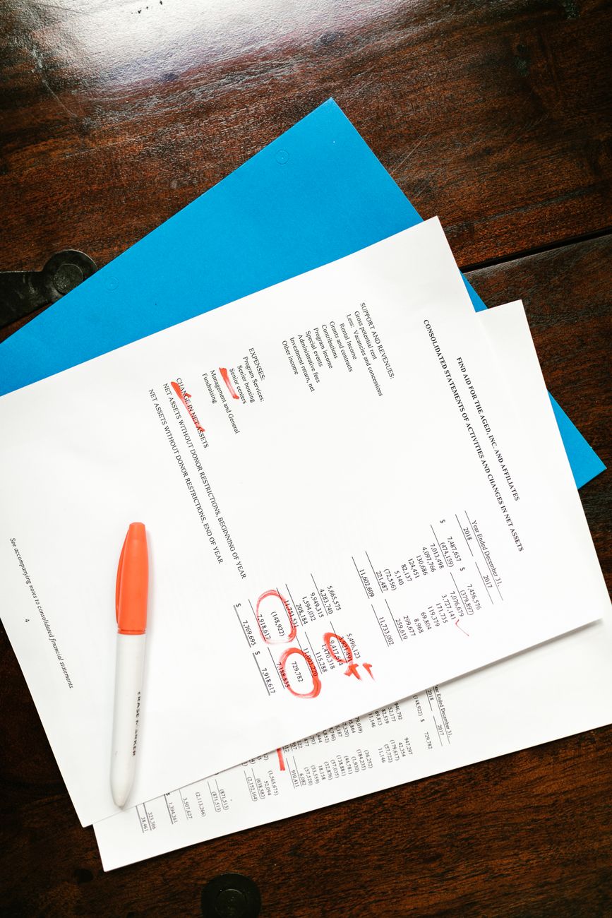A printed multi-page credit report lying open on a wooden desk in one-sided window light, several lines marked